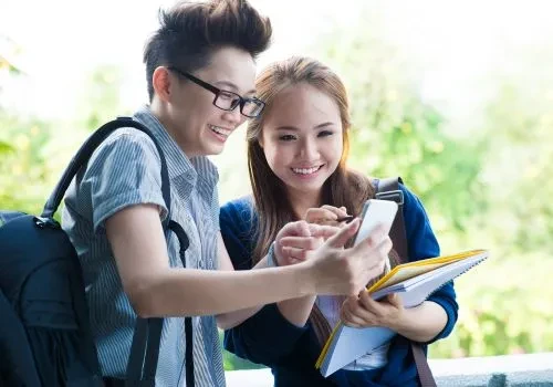 Some students laughing while looking at a game on a cellphone